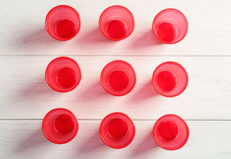 Three rows of red plastic cups on a white wooden table, top view.の写真素材