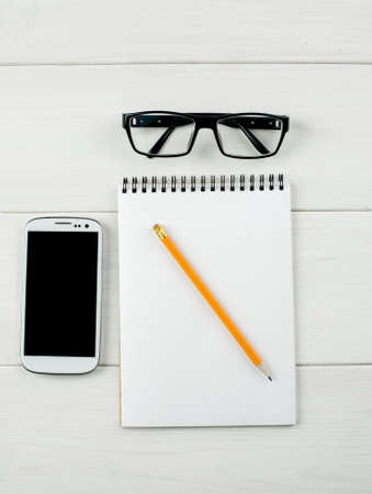 Top view of an office workspace with glasses, smartphone and notepad with pencil.の写真素材