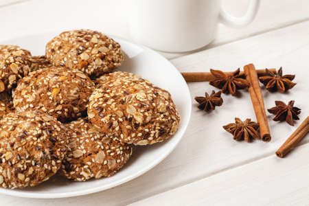 Homemade oatmeal cookies with sesame, nuts and seeds with cinnamon and star anise on a white wooden table.の写真素材