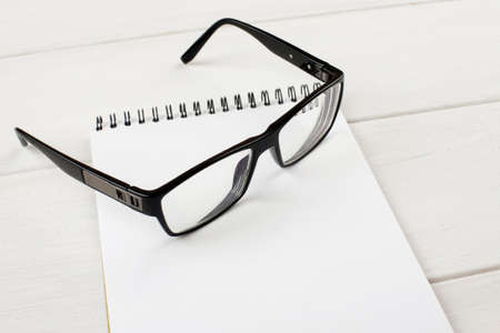 Open notepad with black-rimmed eyeglasses on a wooden table.の写真素材