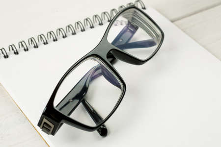 Black-rimmed glasses laying on a notepad blank sheet on a wooden table.