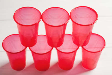 Stacked red plastic cups on a white wooden table.の写真素材