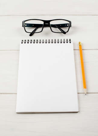 Eyeglasses and notepad with pencil on a white wooden table, vertical.の写真素材