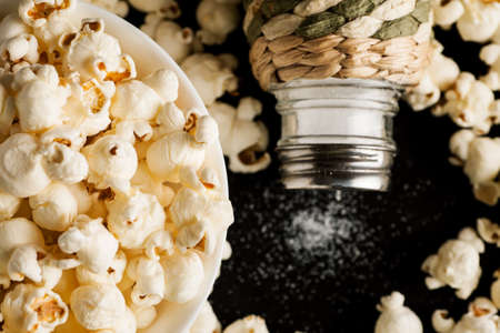 Popcorn in white ceramic bowl with salt shaker on a black wooden table, top view.の写真素材