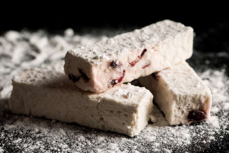 White turkish delight with berries in it on a black surface sprinkled with powdered sugar.の写真素材