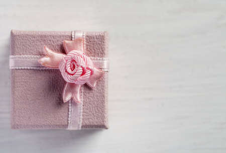 Small pink gift box with bow on a white wooden table, text space, top view.の写真素材