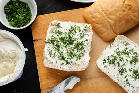 White bread with curd cheese and fresh dill on a wooden table, top view.
