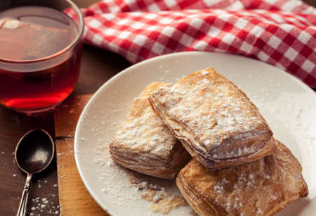 Puff pastries in a white plate with cup of red herbal tea on a wooden table, selective focus.の写真素材