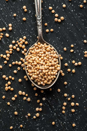 White mustard seeds in metal spoon on a black wooden table, selective focus, top view, flat lay, vertical.の写真素材