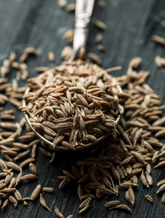 Cumin dry seeds in metal spoon on a black wooden table, macro shot.の写真素材