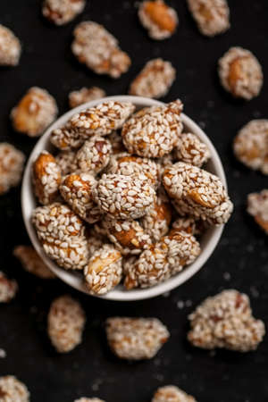 Closeup shot of peanuts covered with sesame in white bowl on a black wooden table, vertical.の写真素材