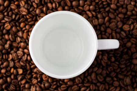 Empty white mug among coffee beans, top view.の写真素材