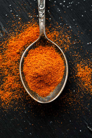 Paprika powder in a metal spoon on a black table, top view, flat lay, vertical.の写真素材