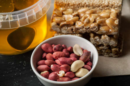 Raw peanuts in ceramic bowl and honey jar on a black wooden table.の写真素材
