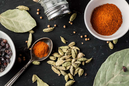 Ground paprika, cardamon seeds and other condiments on a black wooden table, top view, flat lay composition.の写真素材