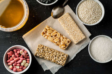 Honey jar, peanuts, sunflower seeds in white ceramic bowls and some brittle on a wooden table, top view, flat lay.の写真素材