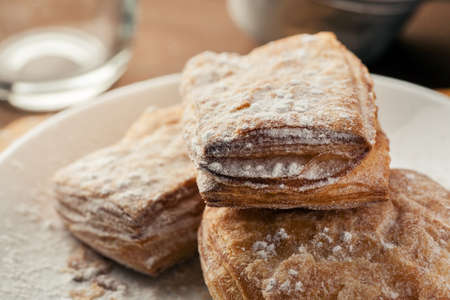 Puff pastry dusted with powdered sugar in a white plate, macro shot.