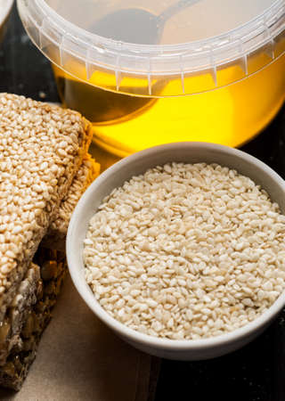 Sesame seeds in a white ceramic bowl and few brittle with honey jar, closeup shot, vertical.の写真素材