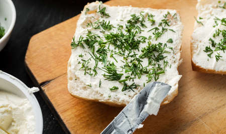 Piece of white bread covered with cream cheese and sprinkled with fresh green dill, selective focus.