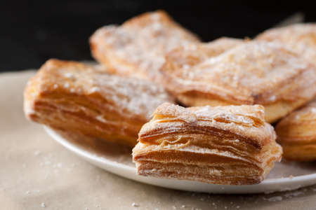 Macro shot of puff pastries dusted with powdered sugar in white plate.
