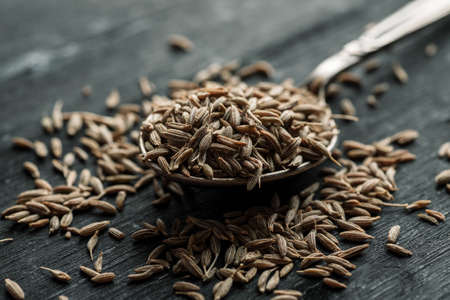 Cumin dry seeds in metal spoon on a black wooden table.の写真素材