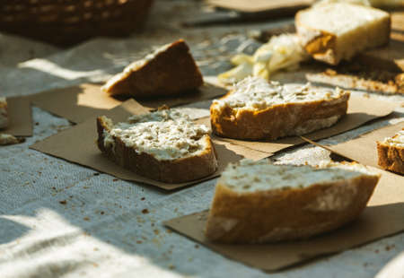 Pieces of fresh bread with some spread on it and craft paper under, warm sunlight.の写真素材