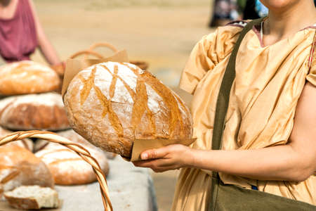 Bread seller woman holding big round loaf of bread in her arms.