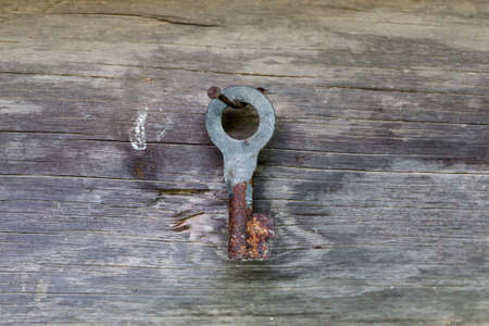 Old metal rusted key hanged on a gray wooden wallの写真素材