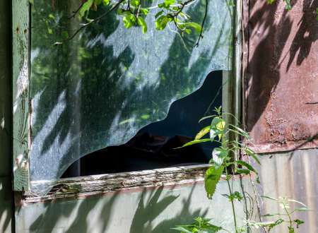 Broken window in abandoned trailer among high grass in sunny day