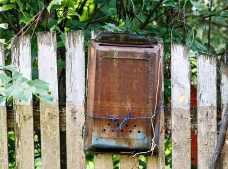 Old metal rusted mail box hanged on a wooden fence under green treeの写真素材