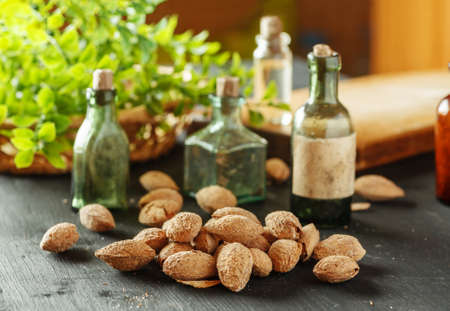 Pile of almond in shell with old small glass bottles on a black table and greenery in the backgroundの写真素材
