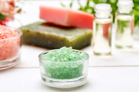Green sea salt in a small glass bowl, handmade soap and few small bottles with liquid inside behind on a white wooden tableの写真素材
