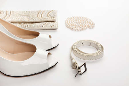 Female white shoes, bag, belt and pearl necklace on a white background