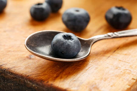 Big fresh ripe blueberry in a metal spoon on a wooden table, closeup shotの写真素材