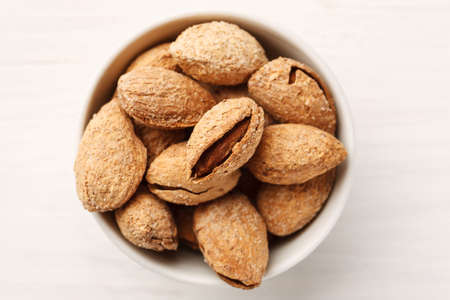 Almond in shell in a white ceramic bowl, top view, flat lay