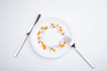 Different medications in a white plate with metal knife and fork on a white backgroundの写真素材