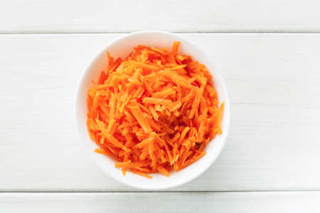 Grated fresh carrot in a white ceramic bowl top viewの写真素材