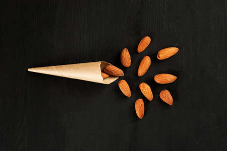 Paper cone bag with almond on a black wooden board, top view flat layの写真素材
