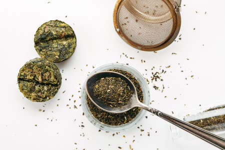 Dry green tea in a metal spoon with compressed tea near on a white background, top viewの写真素材