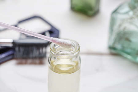 Open glass small bottle with cotton swab above it among cosmetic makeup items on a white wooden table, closeup shot, selective focusの写真素材