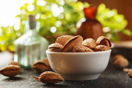 Almond in shell in a white ceramic bowl on a black wooden table with vintage glass bottles and greenery in the backgroundの写真素材