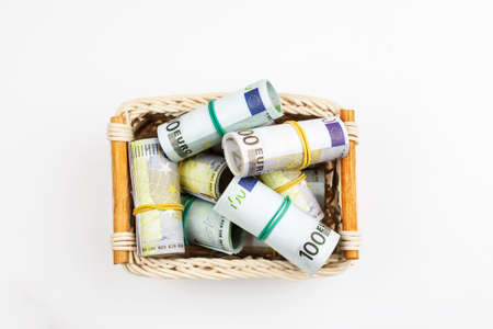 Pile of euro banknotes in rolls in a wicker basket on a white backgroundの写真素材