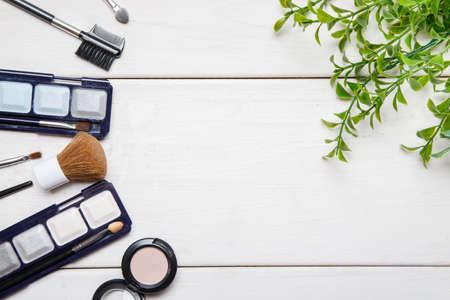 Cosmetic makeup items and green plant branch on a white wooden table, flat lay template with text space in the middleの写真素材