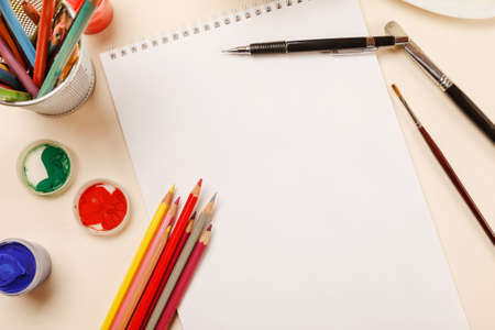 Blank sheet of paper, pencils, paint jars on a table, top viewの写真素材