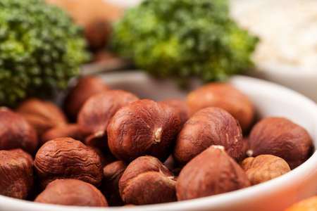 Fresh raw nuts in white bowl among greenery and vegetables, macro shotの写真素材