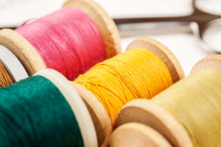 Different colour thread on wooden spools on a white background, macro shot