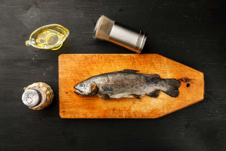 Fresh fish with herbs and spices on vintage cutting board on dark background, top viewの写真素材