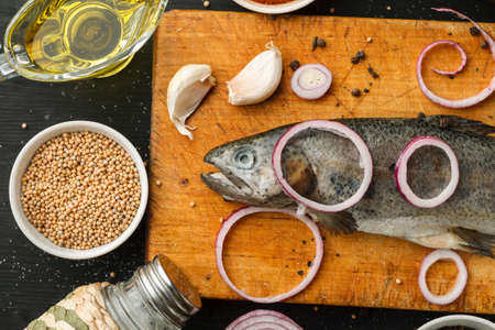 Fresh fish with herbs and spices on vintage cutting board on dark background, top viewの写真素材