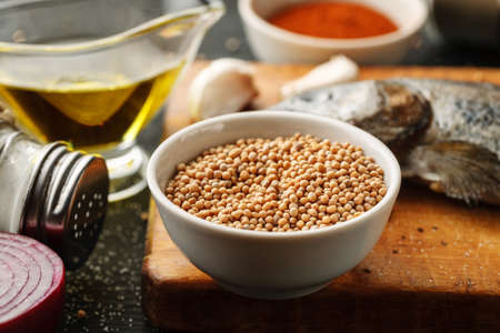 White mustard seeds in a white ceramic bowl on a wooden cutting board. Cooking processの写真素材
