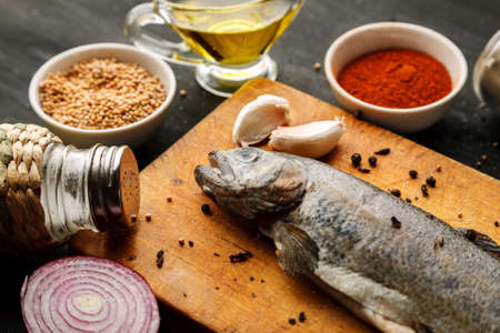 Fresh fish with herbs and spices on vintage cutting board on dark backgroundの写真素材